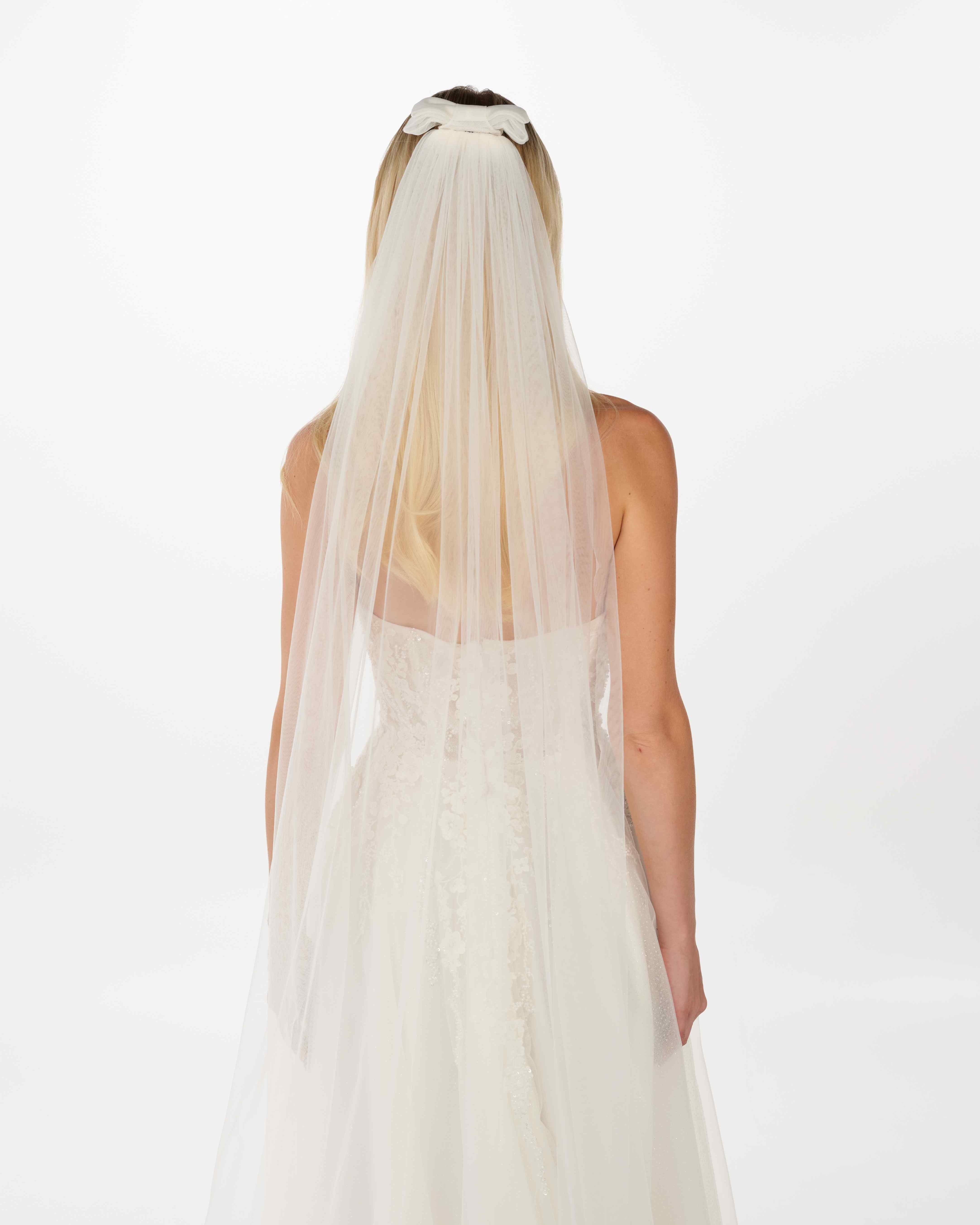 EIne Braut mit offenen Haaren, einem cleanen Kleid trägt einen Bun eine Tüllschleife und einen Schleier