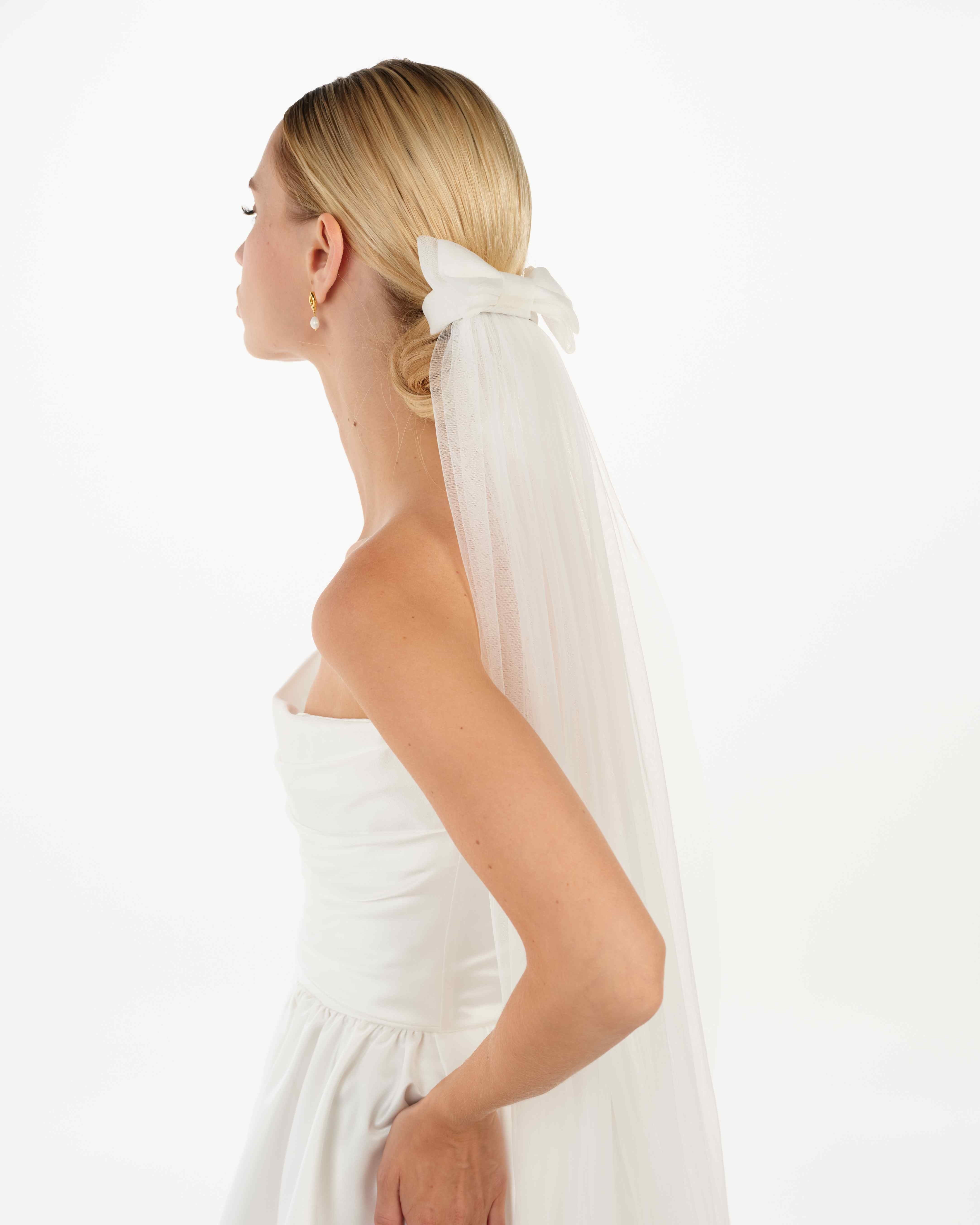 EIne Braut mit cleanen Bun trägt eine Tüllschleife und einen langen Schleier