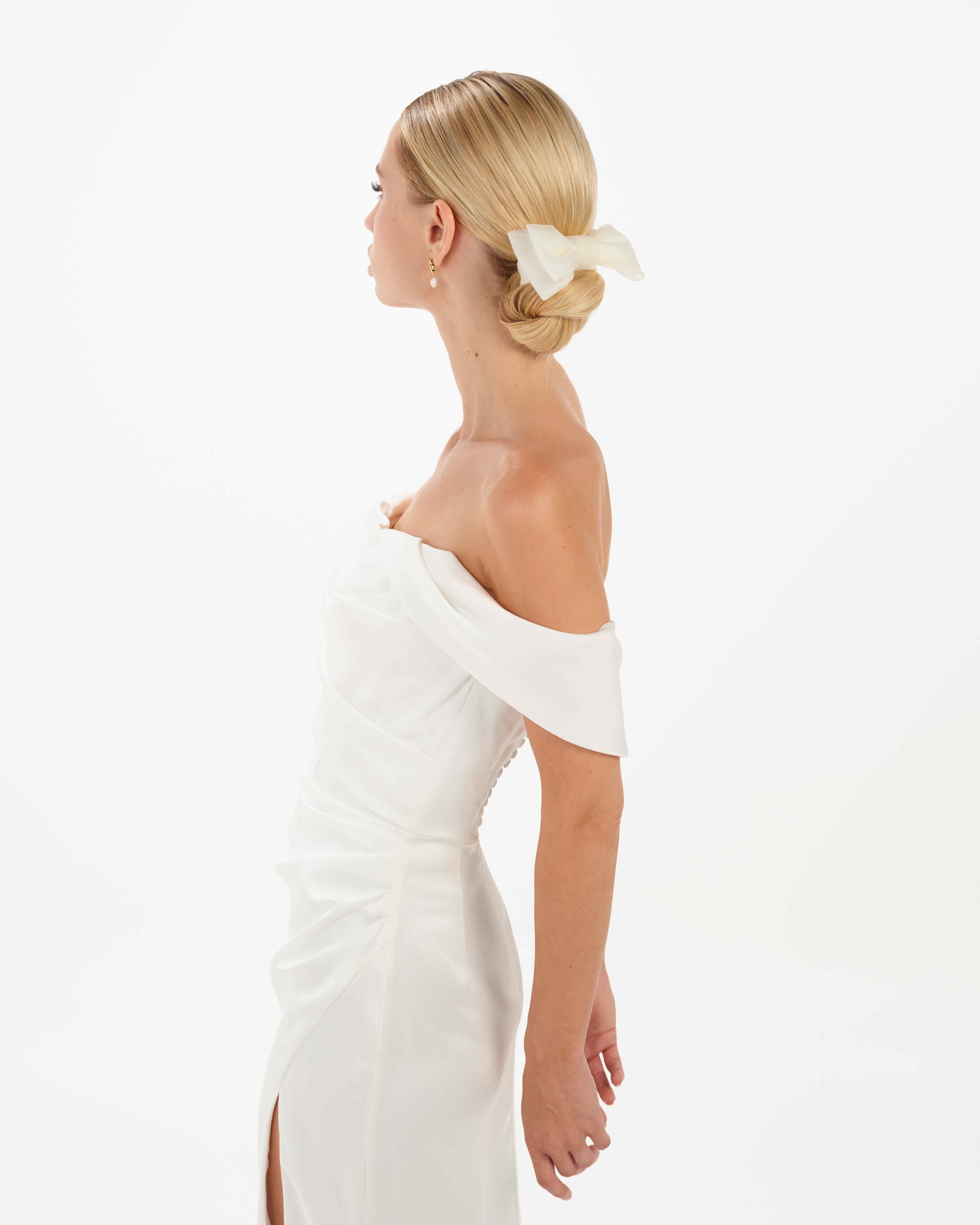 EIne Braut mit cleanen Bun,. einem cleanen Kleid trägt einen Bun eine Tüllschleife