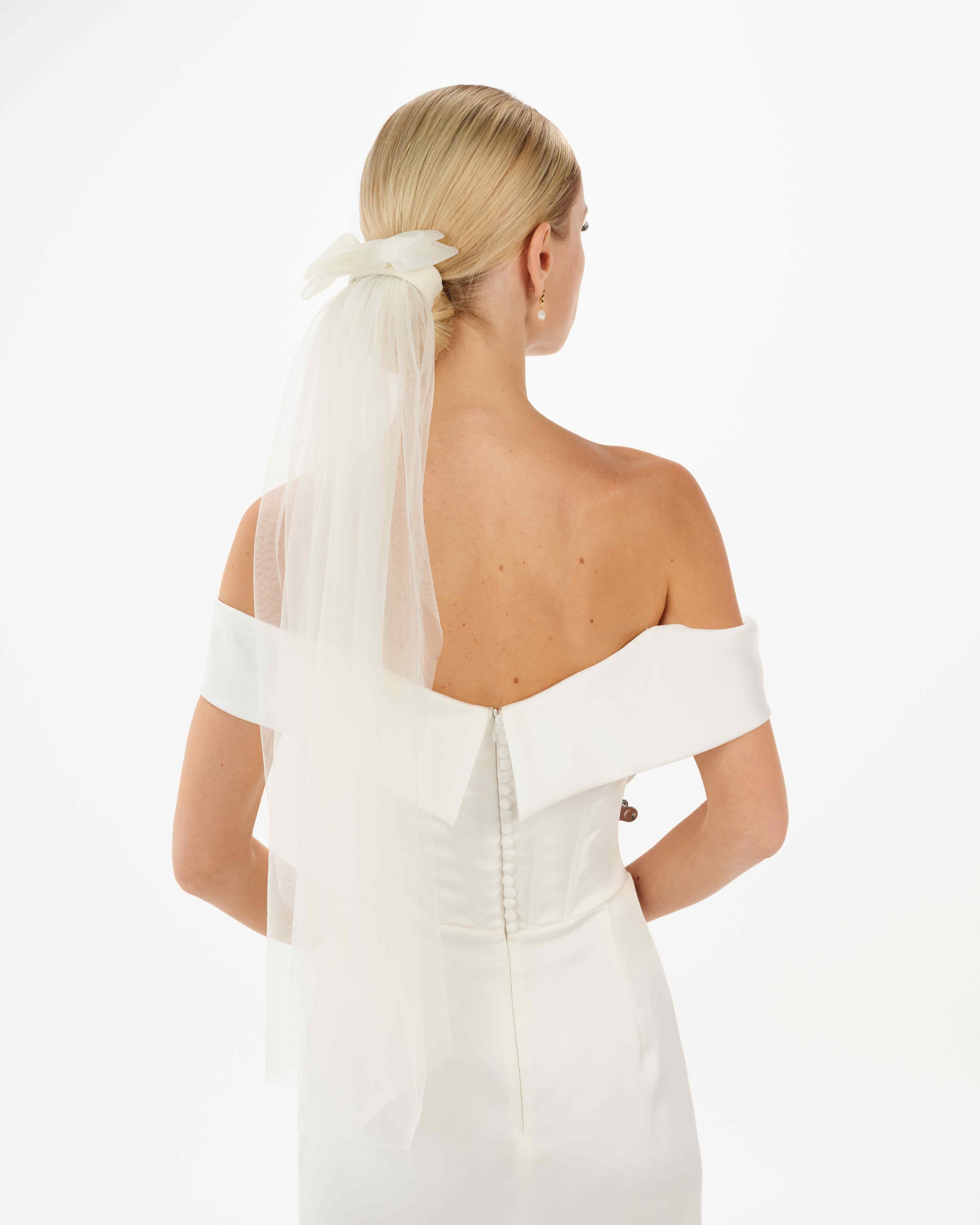 EIne Braut mit cleanen Bun trägt eine Tüllschleife, Tüllhaarband und einen Schleier