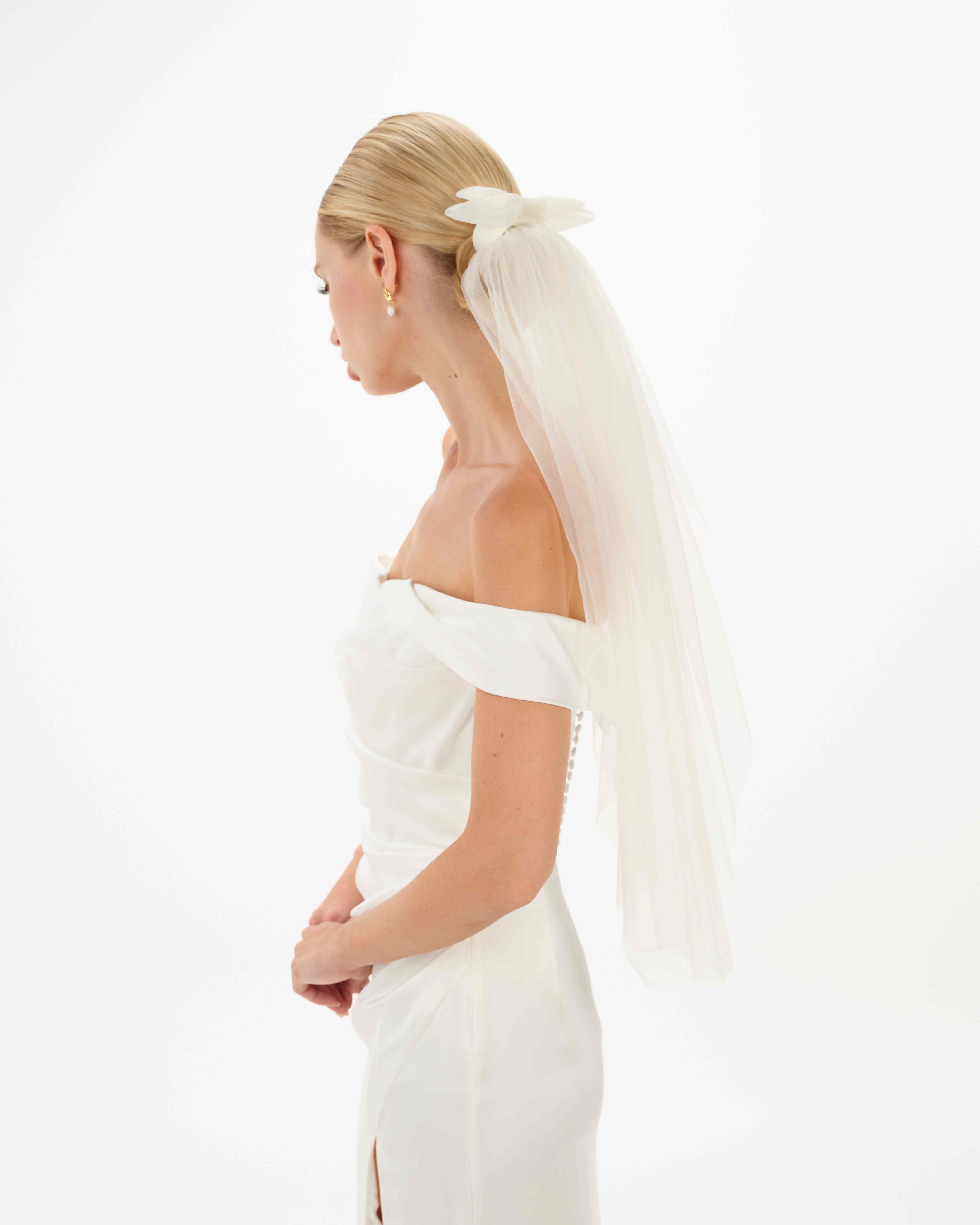 EIne Braut mit cleanen Bun trägt eine Tüllschleife, Tüllhaarband und einen kurzen Schleier