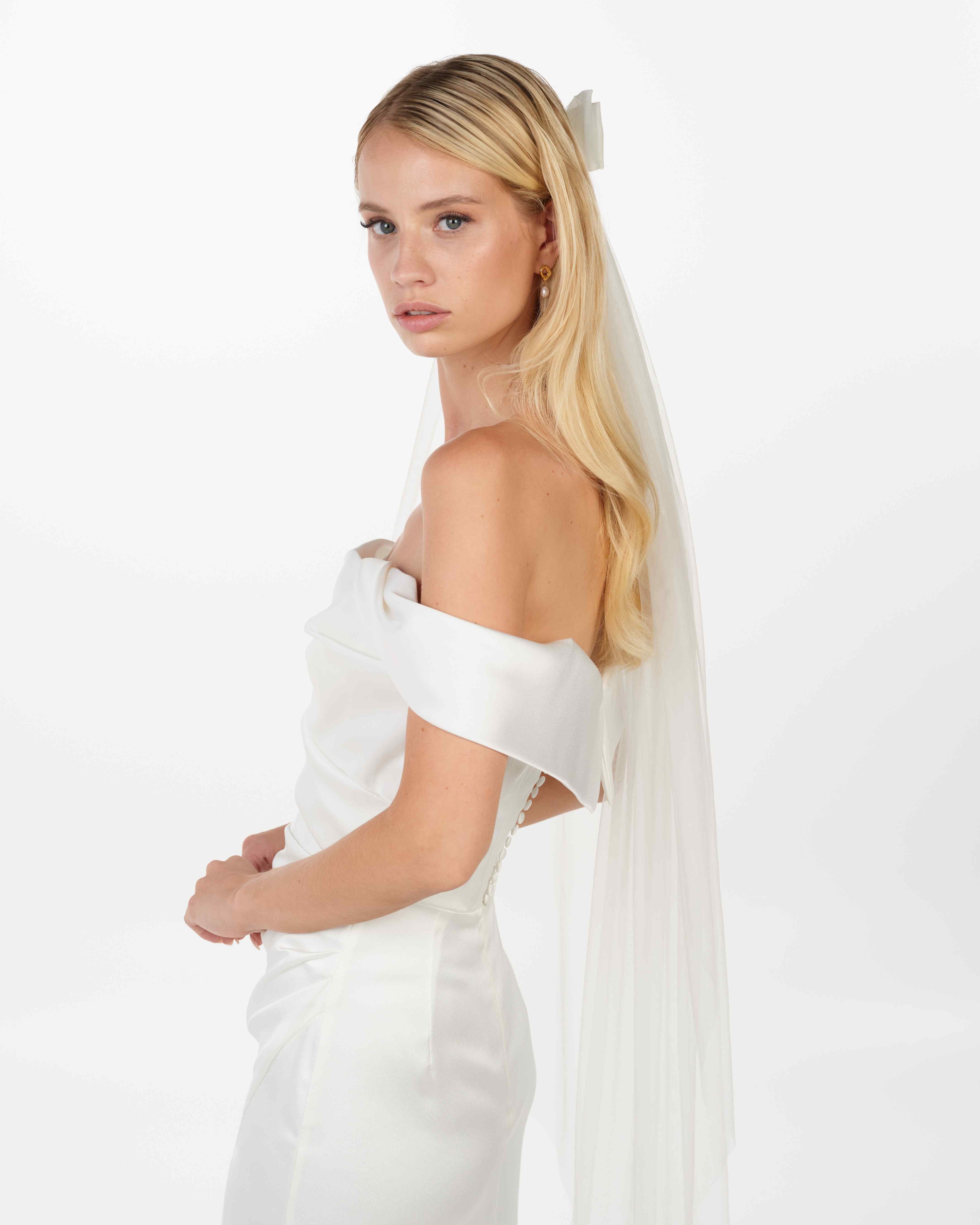 EIne Braut mit offenen Haaren, einem cleanen Kleid trägt einen Bun eine Tüllschleife und einen Schleier