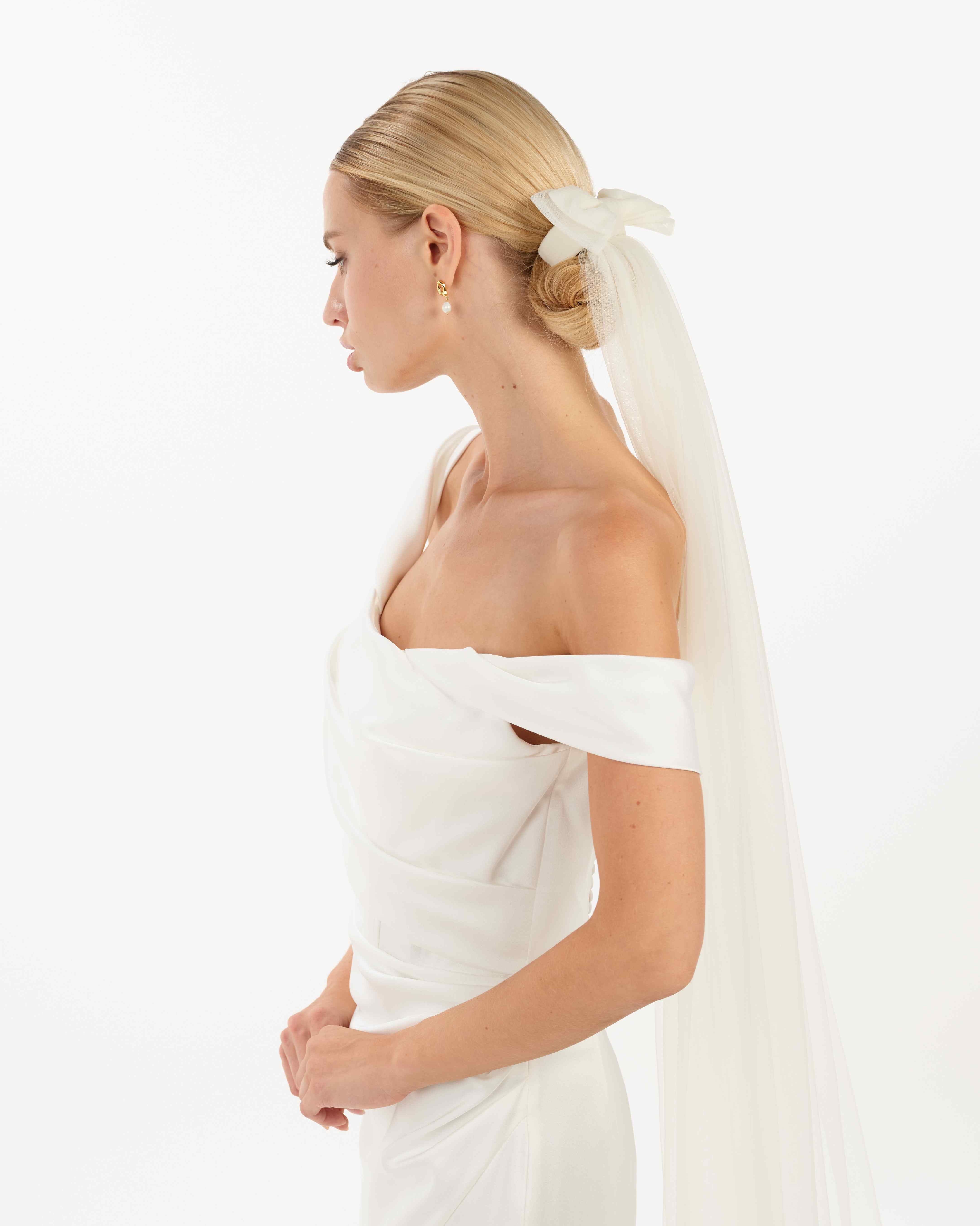 EIne Braut mit cleanen Bun trägt  eine Tüllschleife, Tüllhaarband und einen Schleier