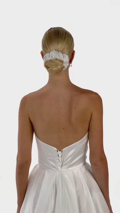 Eine Braut mit einem gerafften Seiden-Haarband im Bun dreht sich von hinten nach vorne