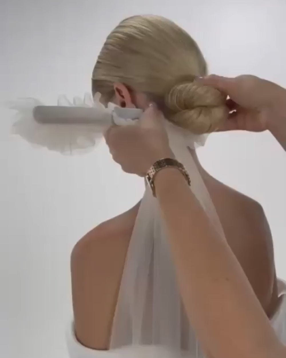 Einer Braut mit cleanen Bund wird ein gewelltes Tüll-Haarband und Schleier in die Frisur eingesetzt