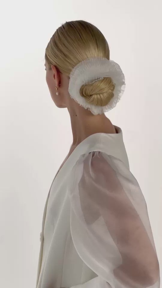 Eine Braut mit gerafften Tüll-Haarband im Bun dreht sich von vorne nach hinten