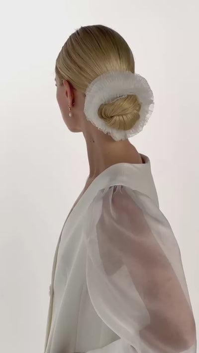 Eine Braut mit gerafften Tüll-Haarband im Bun dreht sich von vorne nach hinten