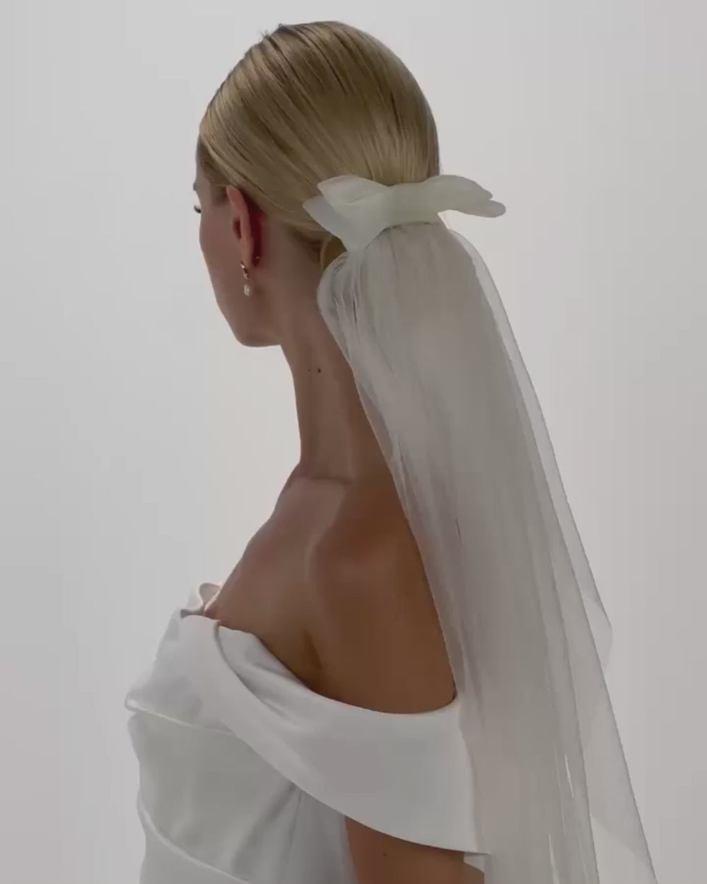 EIne Braut mit cleanen Bun, einem Tüll-Haarband, einer Tüllscleife und einem Schleier dreht sich von hinten nach vorne